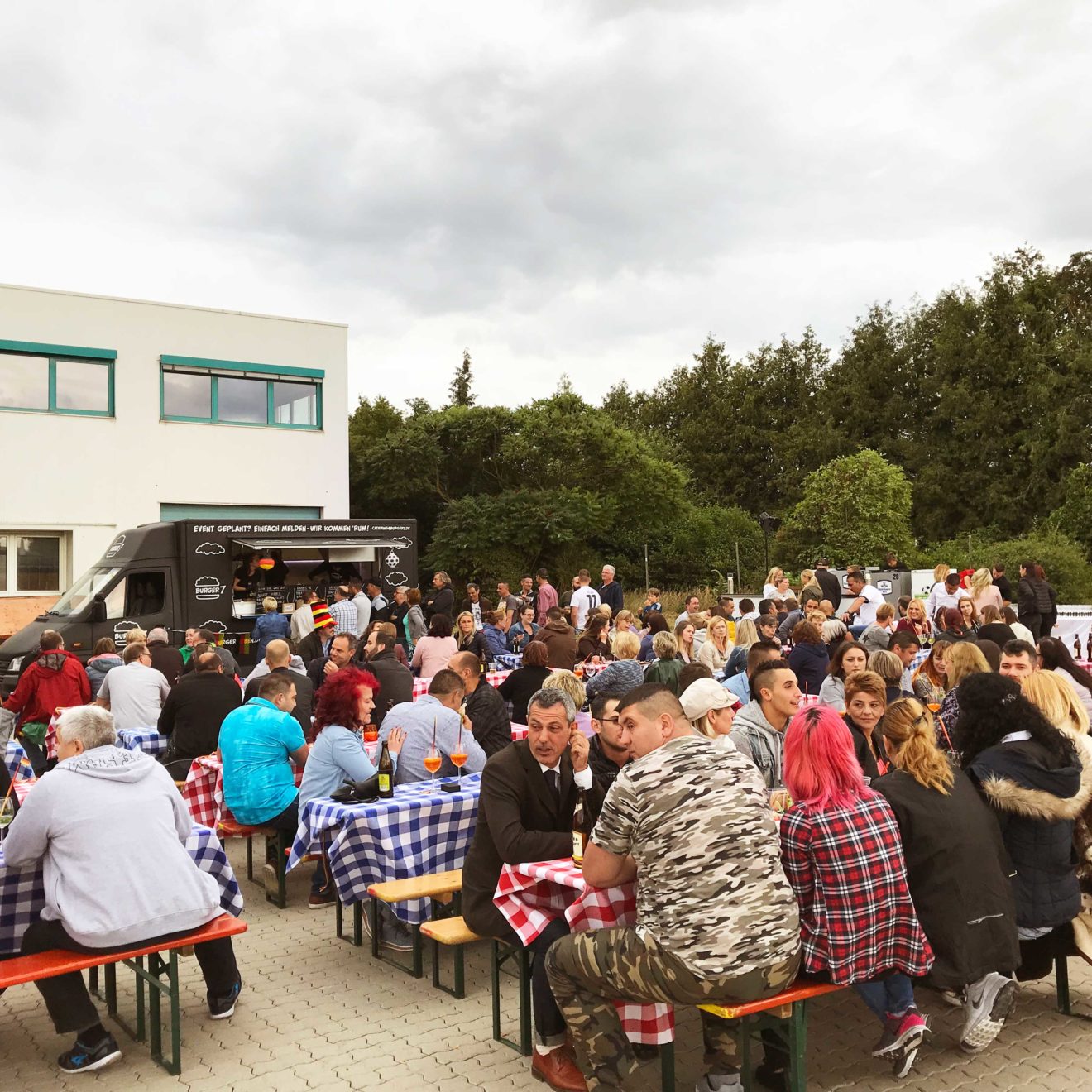 Eventorganisation: Außenansicht Eventlocation mit Gästen und Foodtrucks